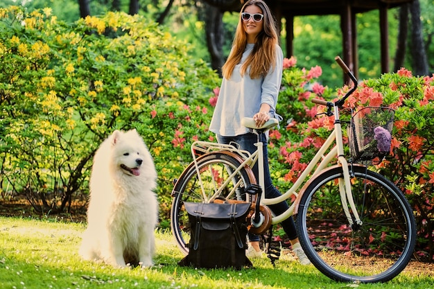 A girl with her dog and a bicycle on a background in a park.