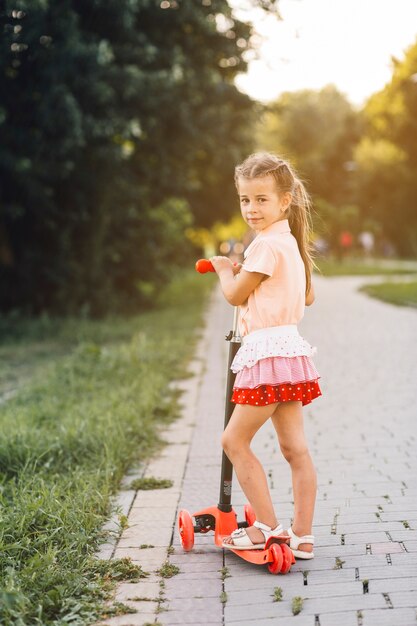 公園に立っている彼女のプッシュスクーターの女の子