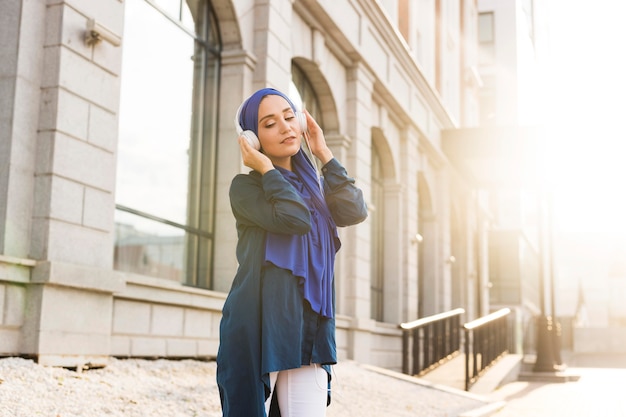 Girl with hijab listening to music through headphones outdoors