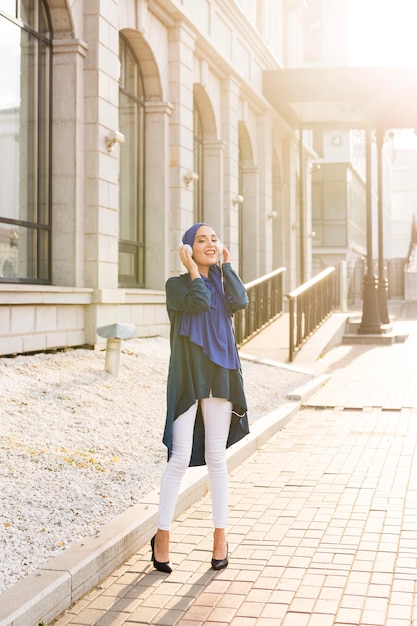 Girl with hijab listening to music through headphones outside