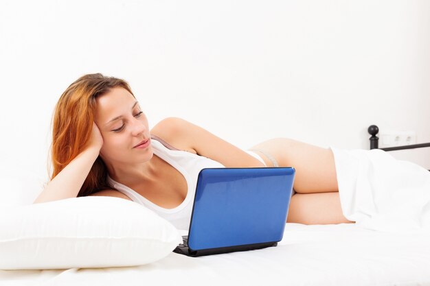 girl with laptop lying on white sheet in her bed