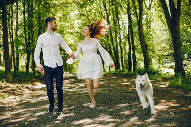 흰 드레스를 입고 가벼운 머리를 가진 여자는 그녀의 강아지와 남자 친구와 함께 놀고있다