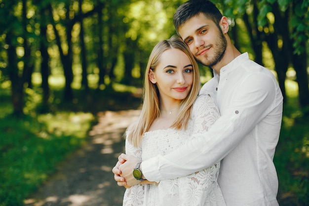 girl with light hair and a white dress is walking in a sunny forest with her boyfriend