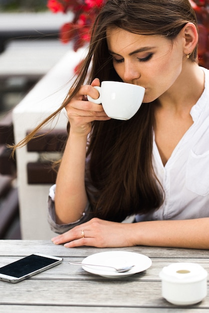 Девушка с длинными волосами выпивает кофе, сидя в ресторане