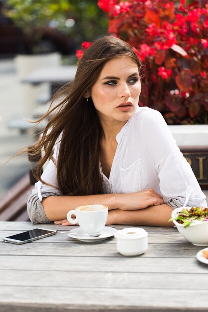긴 머리를 가진 여자는 레스토랑에 앉아 커피를 마신다