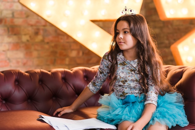 Girl with long hair wearing crown sitting on sofa with scripts