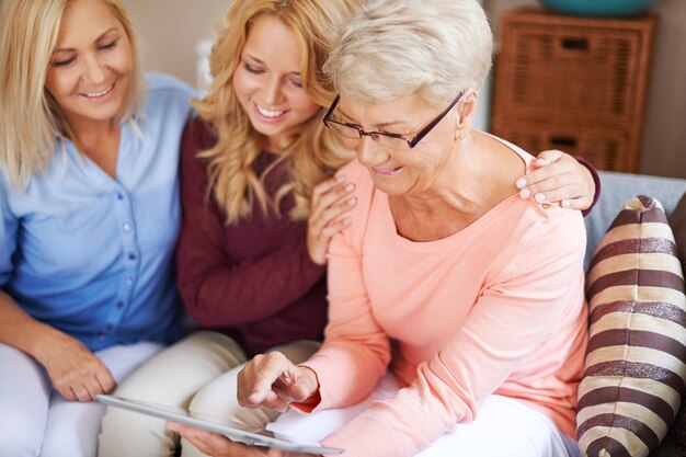 Девушка с мамой поддерживает бабушку, которая учится на цифровом планшете