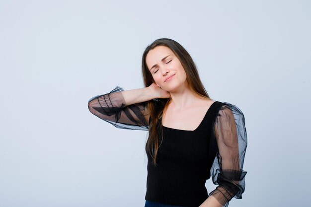 Girl with neckache is putting hand behind neck on white background