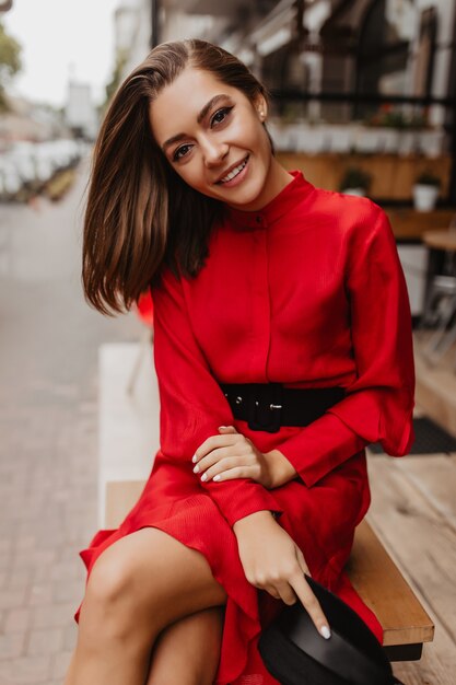 Girl with nude makeup bowed her head and smiles sweetly. Full-length portrait of Frenchwoman with short stylish haircut, who takes off her black hat