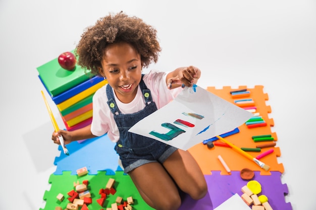 Free photo girl with painted paper on play mat in studio