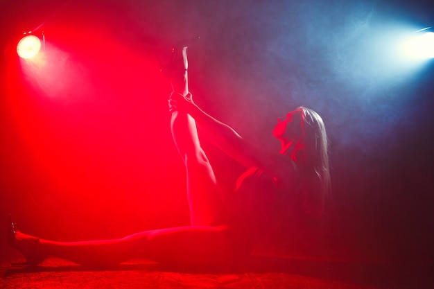 Girl with perfect slim body. Woman posing in bodysuit in red light in the smoke. 