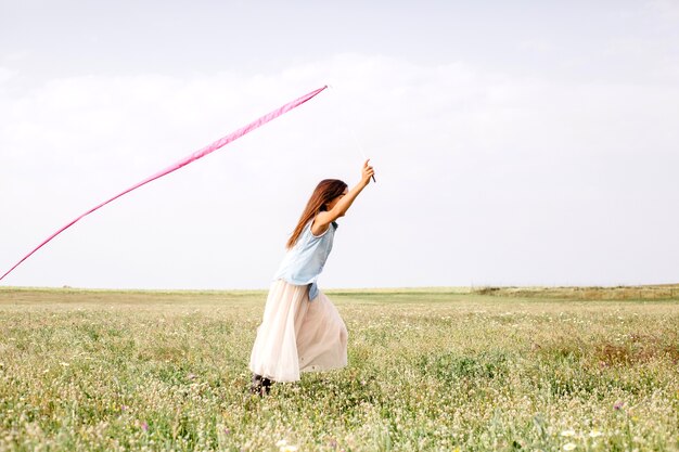 Girl with pink ribbon running in field