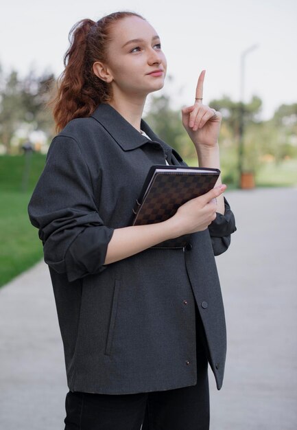 Girl with red hair standing in park pointing by finger