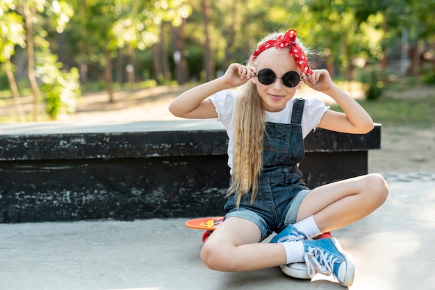 スケートボードの上に座って赤いカチューシャを持つ少女