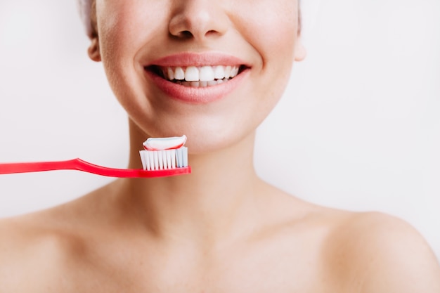 Girl with sincere smile makes morning routine and brushes her teeth on isolated wall.