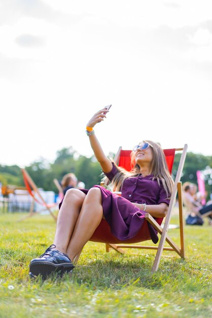 스마트폰과 야외용 데크 의자에 칵테일을 들고 있는 어린 소녀. 여름휴가.