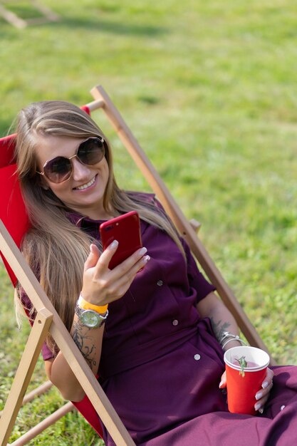 스마트폰과 야외용 데크 의자에 칵테일을 들고 있는 어린 소녀. 여름휴가.