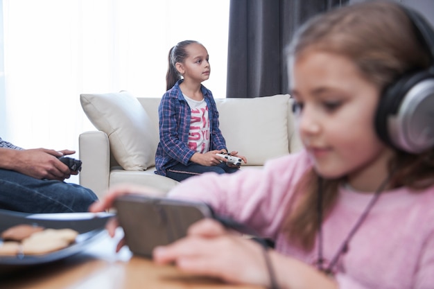 Girl with smartphone near siblings playing video gamens