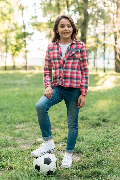 公園で芝生の上に立っているサッカーボールを持つ少女