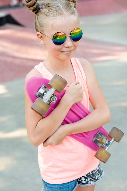 サングラスとピンクのスケートボードを持つ少女