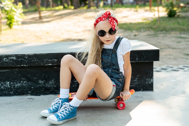 スケートボードの上に座ってサングラスを持つ少女