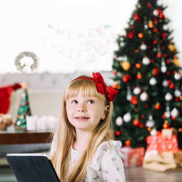 Foto gratuita ragazza con tavoletta davanti all'albero di natale