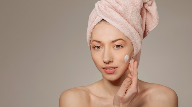 Girl with towel on the head using cream