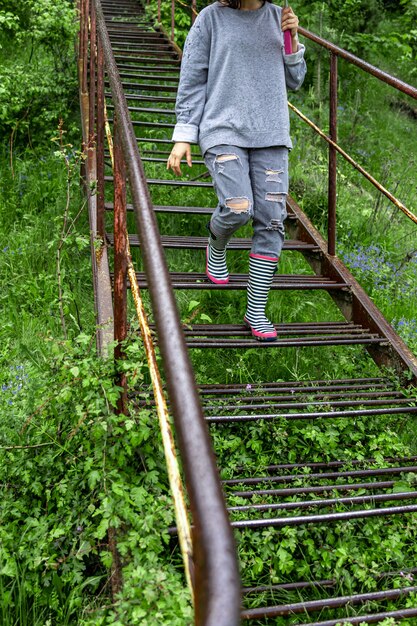 A girl with an umbrella walks in the woods in rainy weather in rubber boots.