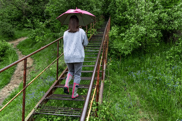 우산을 든 소녀가 비오는 날씨에 숲을 산책합니다.