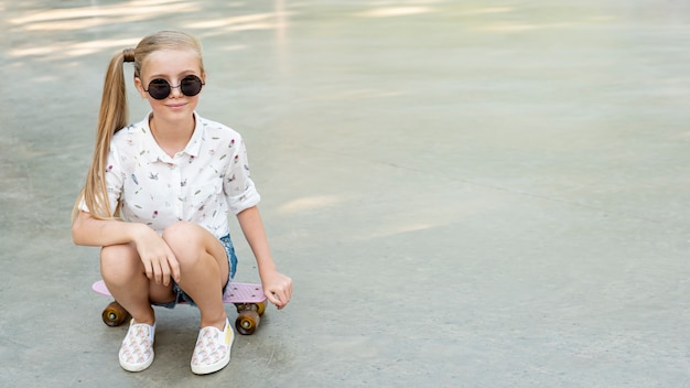 Foto gratuita ragazza con camicia bianca seduto su skateboard