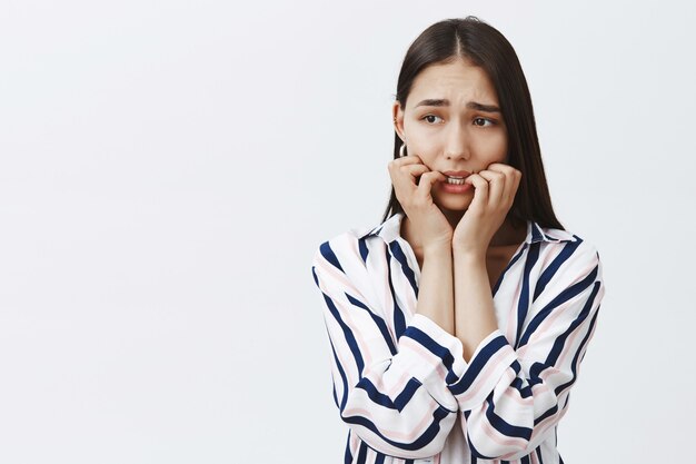 Girl witnessed crime, feeling anxious and afraid. Portrait of innocent gloomy and nervous female in trendy clothes, biting fingernails, frowning and gazing aside, being confused and scared