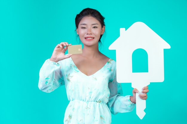 The girl wore a white long-sleeved shirt with floral pattern, holding a white house symbol and a gold credit card with a blue .