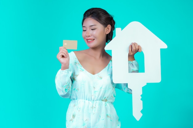 The girl wore a white long-sleeved shirt with floral pattern, holding a white house symbol and a gold credit card with a blue .