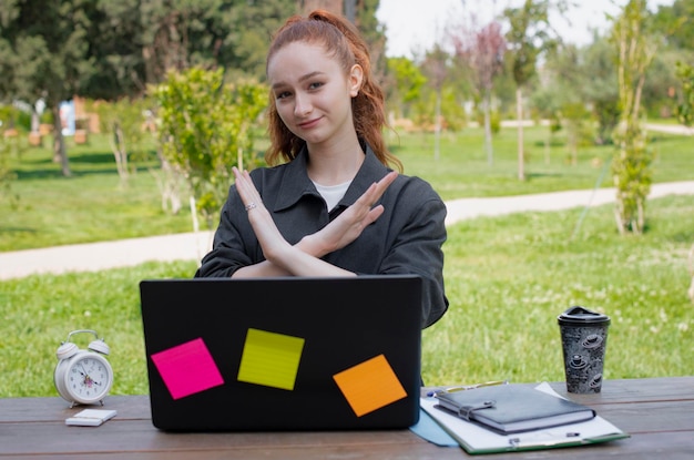 Girl working at laptop showing stop crossing hands outdoors