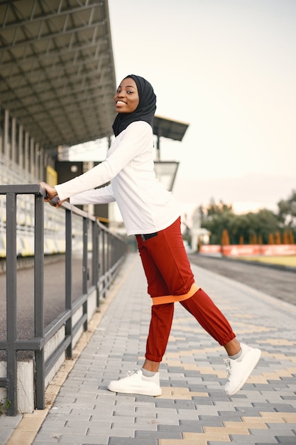 Girl working out outdoors on a stadium. Muslim woman wearing white shirt and red trousers