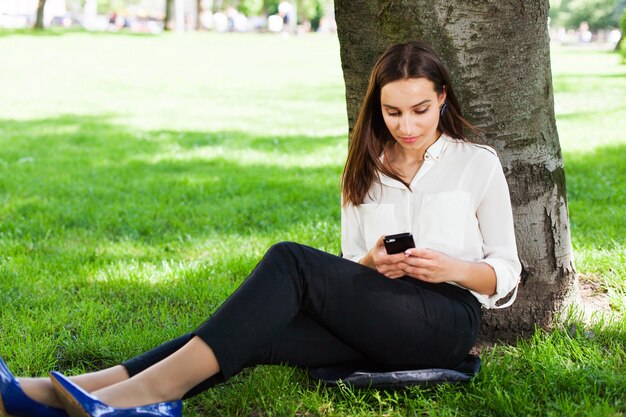 Girl works with her phone sitting under the tree