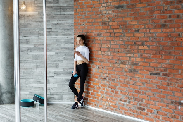 Girl works with her smartphone after or before a work out in the gym