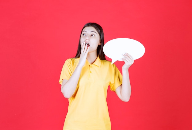 Girl in yellow dresscode holding an ovale info board and looks terrified and stressed