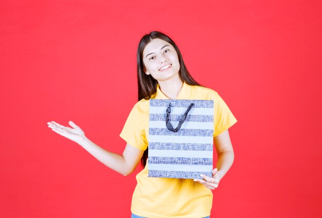 Girl in yellow shirt holding a blue shopping bag with patterns on it