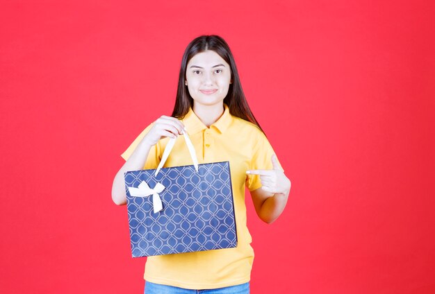 Девушка в желтой рубашке держит синюю сумку для покупок