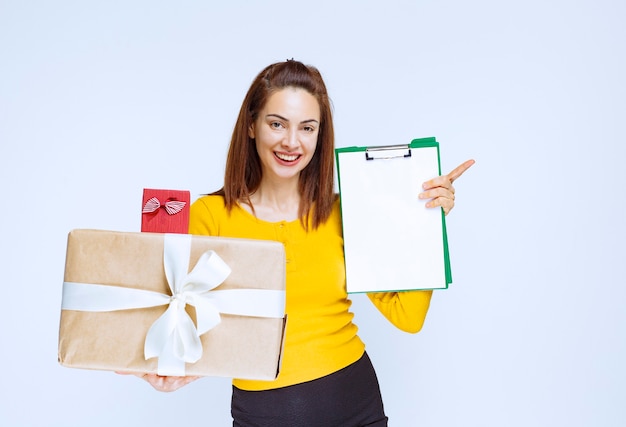 Ragazza in camicia gialla che tiene un rosso e scatole regalo di cartone e chiede una firma.