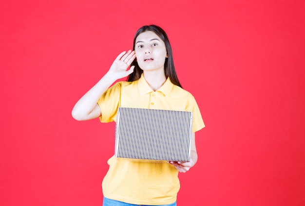 Girl in yellow shirt holding silver gift box and looks confused and thoughtful