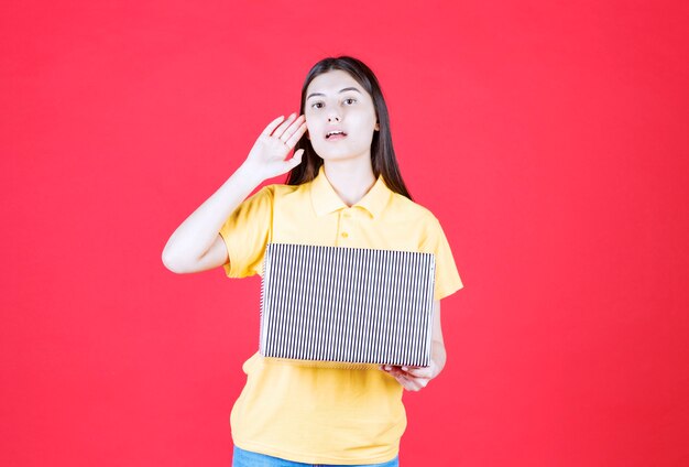 Girl in yellow shirt holding silver gift box and looks confused and thoughtful