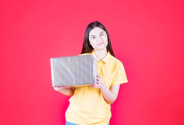 Girl in yellow shirt holding silver gift box.