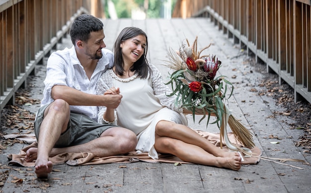 Девушка и молодой человек сидят на мосту и наслаждаются общением, свиданием на природе, историей любви.