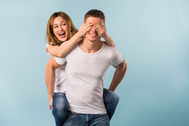 Girlfriend enjoying the piggyback ride on her boyfriend against blue background