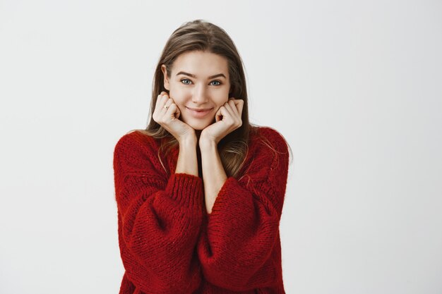 Girlfriend listening incredible story of friend returning from vacation. Indoor shot of joyful charming european woman in loose sweater, leaning head on palms and smiling flirty 