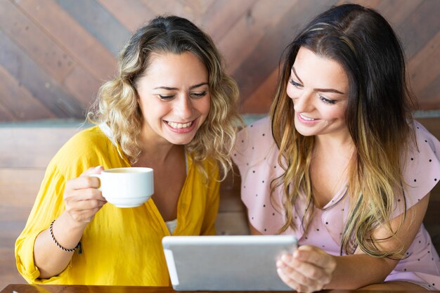 Подруги, используя планшетный компьютер и пить кофе в кафе