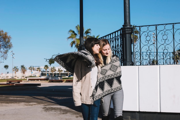 Girlfriends walking on street cuddling in plaid