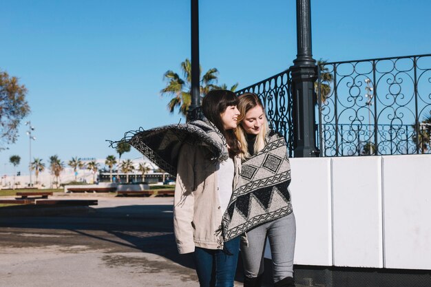 Girlfriends walking on street cuddling in plaid
